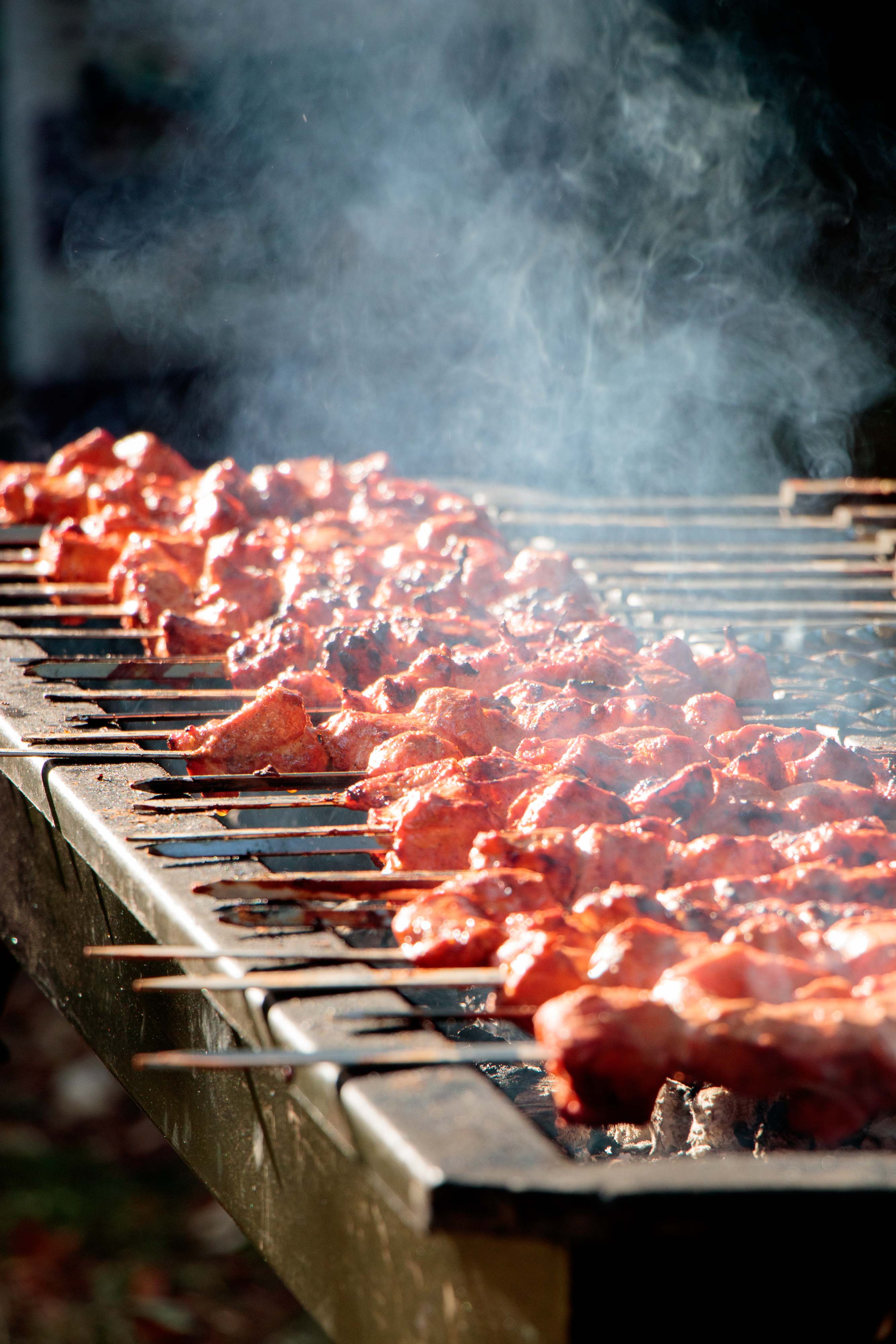 Skewers of marinated tikka grilling over live charcoal with smoke rising